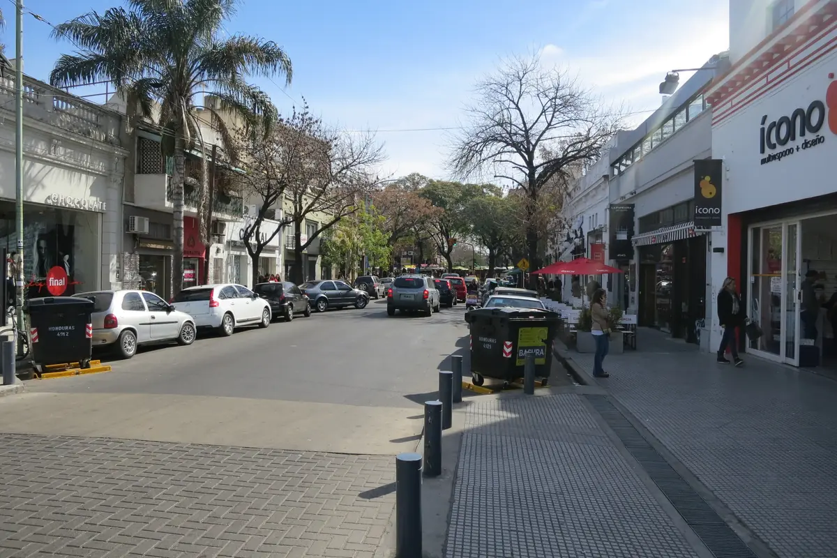 A tree-lined street in Palermo Soho with shops on both sides, cobbled paving and cars parked along the kerb